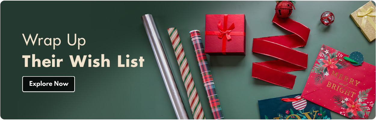 Wrap Up Their Wish List, Christmas gift wrap scene with rolls of festive wrapping paper, ribbon, tags, and wrapped presents on a hunter green background. Explore Now.