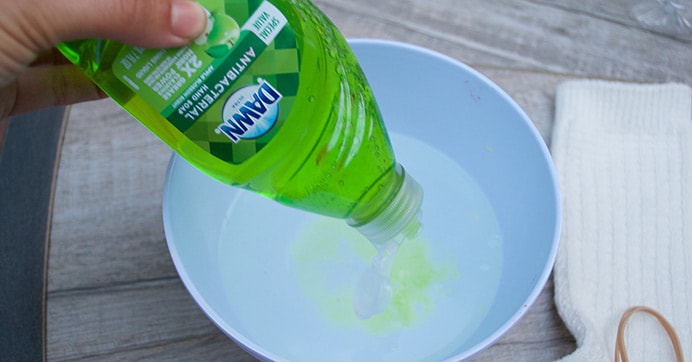 A hand pouring green dish detergent in a white bowl.
