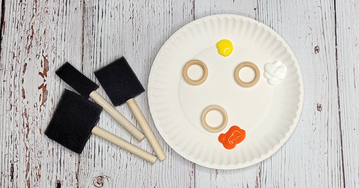 sponge brushes beside a plate with orange, yellow and white paint on it