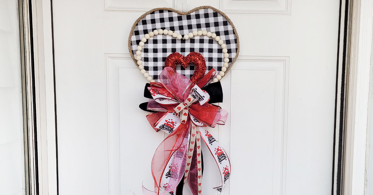 Heartshaped wall decoration covered in black and white plaid fabric, a beaded heart, and a