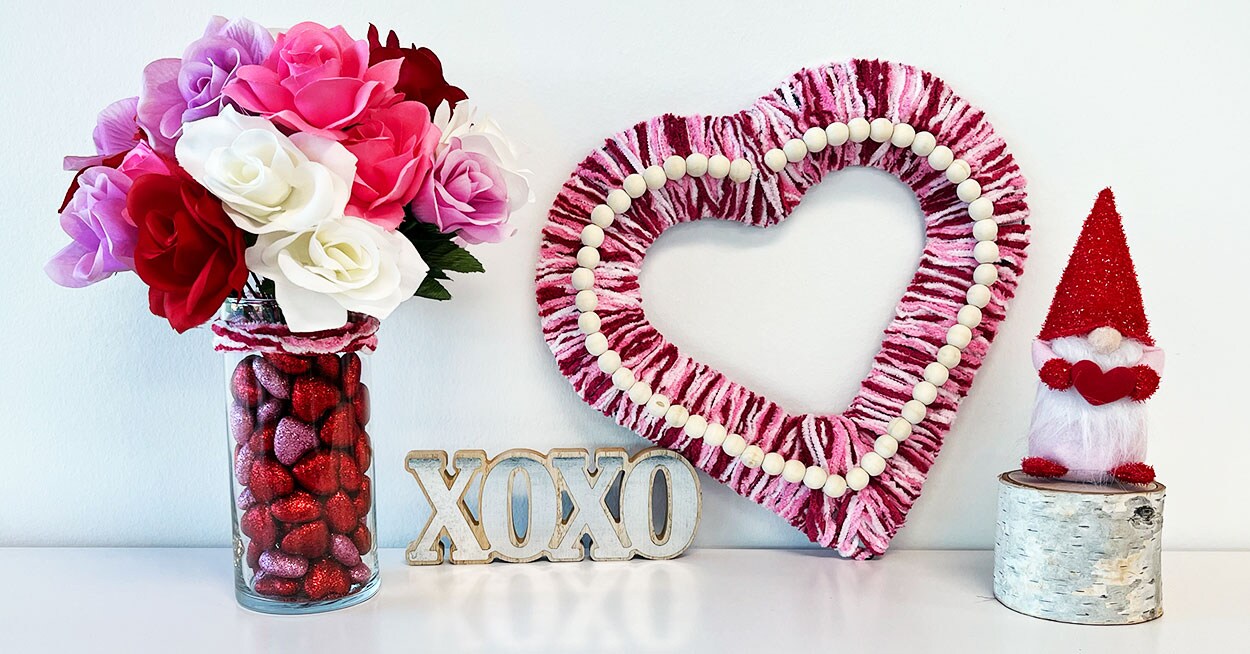 Heartshaped wreath covered in red, pink, and white yarn next to a