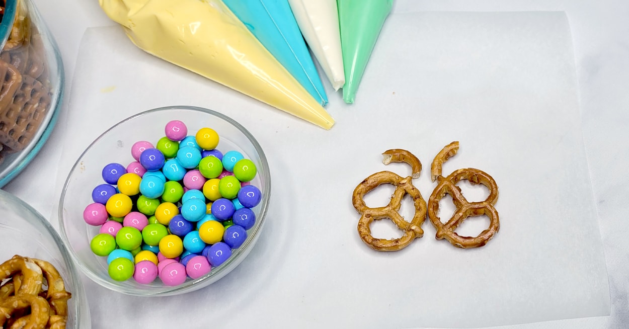 Pastel colored candy in a bowl, icing bags, and a pretzel in the shape