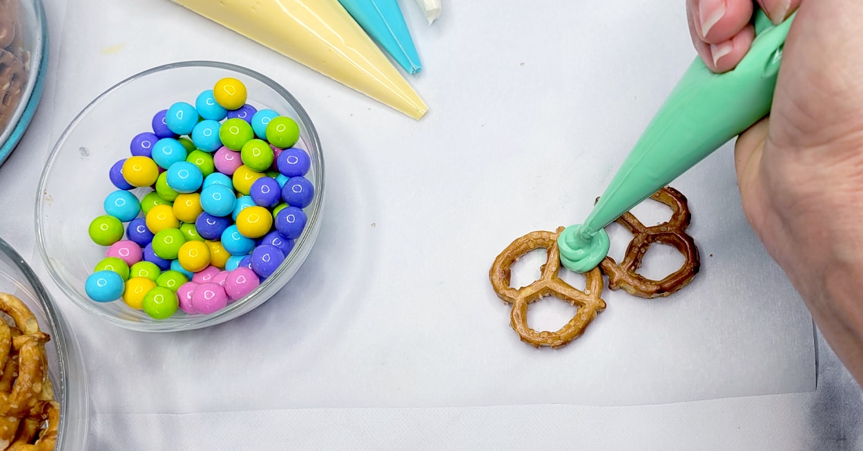 Pastel colored candy in a bowl, and a hand piping green icing onto