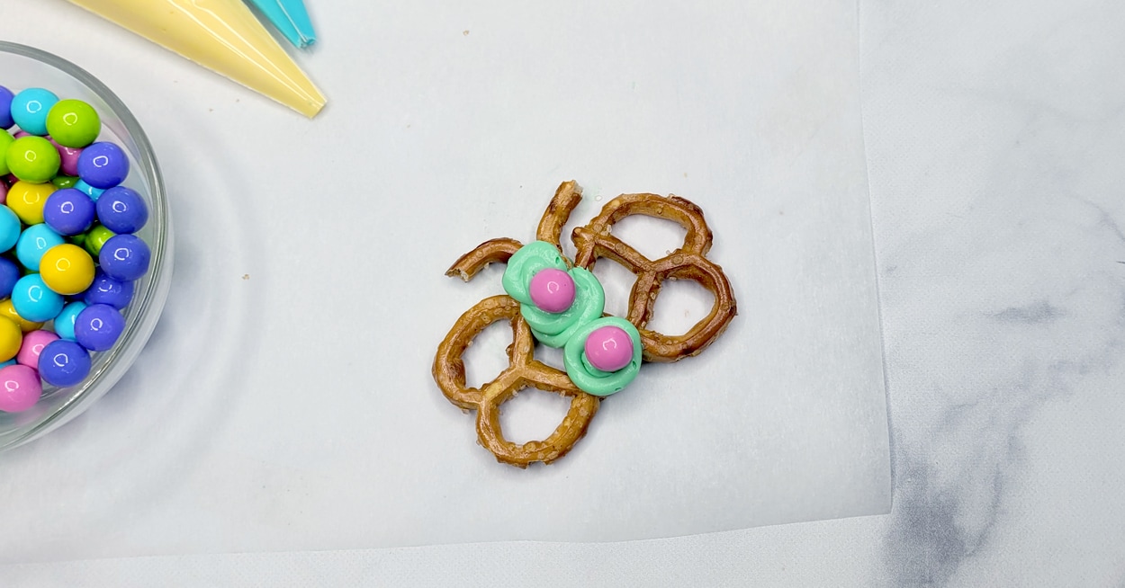 Pastel colored candy in a bowl, and a hand piping green icing onto
