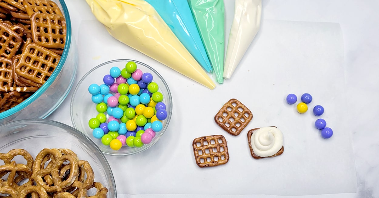 Bowls of pretzels and pastel candies with icing in piping bags.