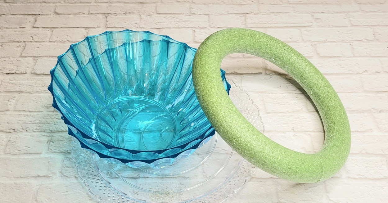 Two blue plastic serving bowls, a foam wreath, and a clear cake plate.