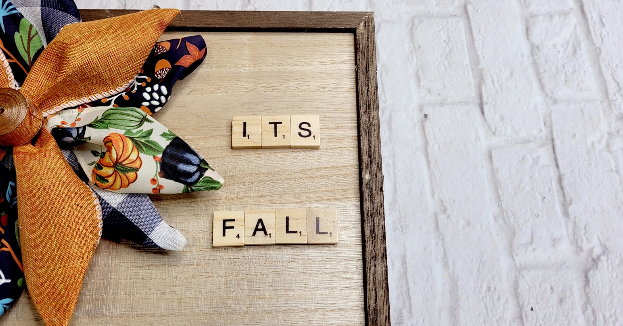 A wooden frame with a ribbon flower on it and letter tiles.