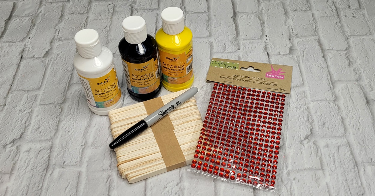 Bottles of white, black, and yellow paint, craft sticks, a black marker