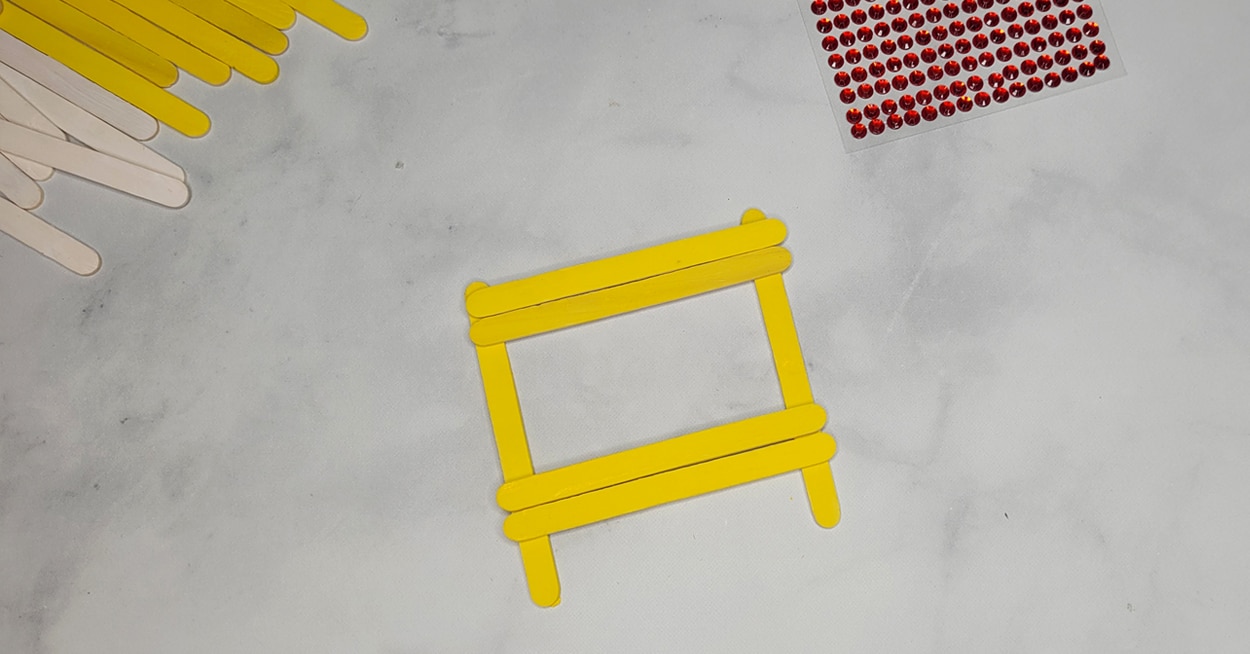 Yellow craft sticks that are glued in a square.