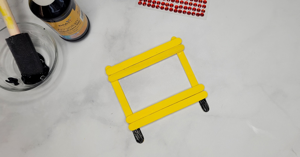 Yellow craft sticks that are glued in a square with a little black on it.