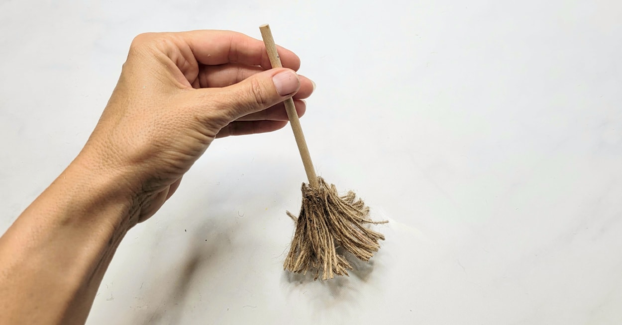 A hand holding a wooden dowel rod with twine on the bottom of it.