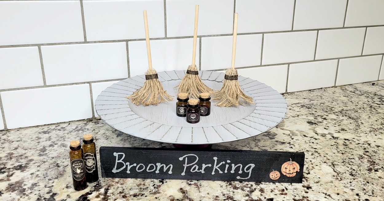 Three DIY witches broomsticks on a tier tray by little poison bottles