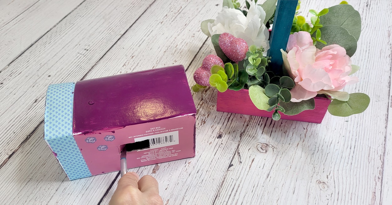 A hand using a craft knife to cut an opening in a decorative mailbox