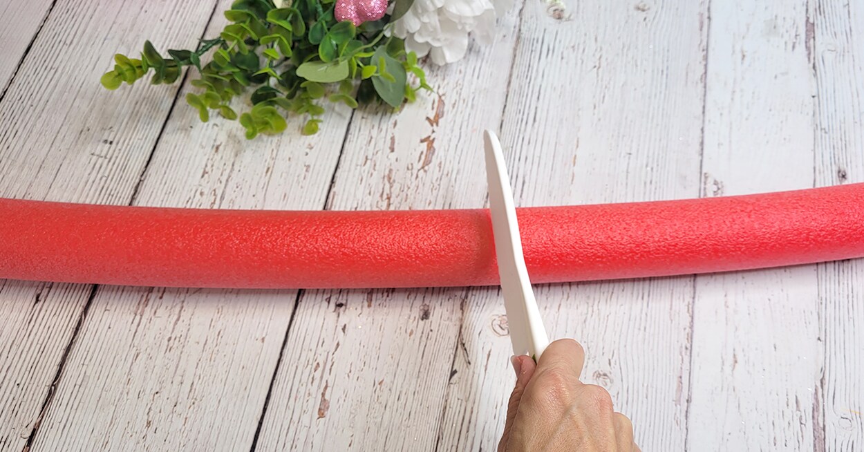 A hand holding a pool noodle knife cutting a red pool noodle.