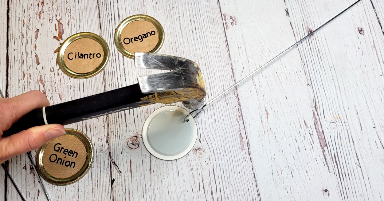 A hand holding a hammer, nailing a nail into a garden stake.