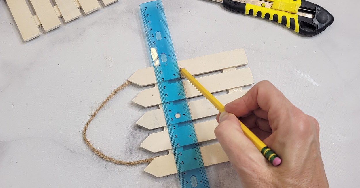 A hand holding a pencil a long a ruler on a small wooden fence.