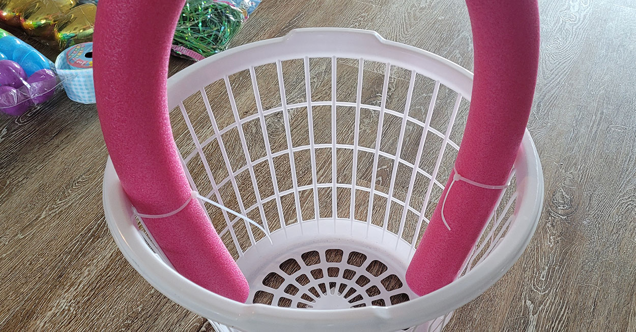 A laundry basket with a pool noodle attached to it and packages of
