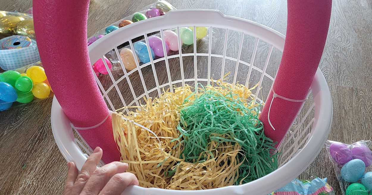 A laundry basket with a pool noodle handle and filled with Easter grass.