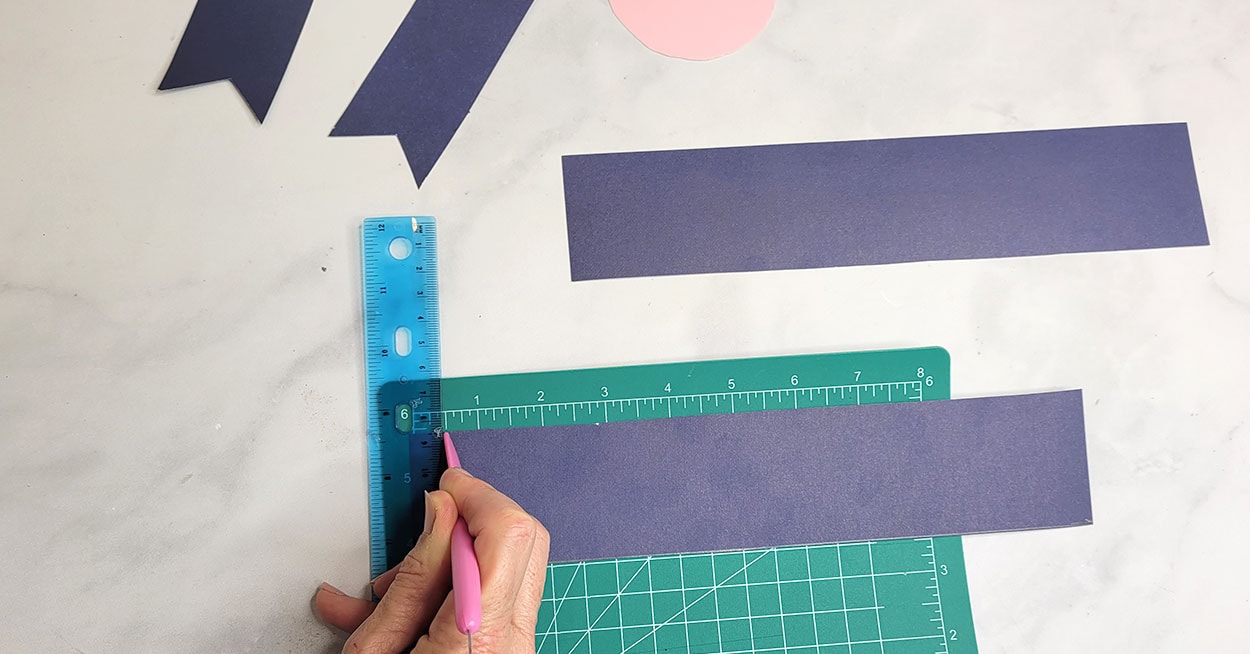 A hand holding a ruler and a pencil on a piece of paper on a cutting pad.